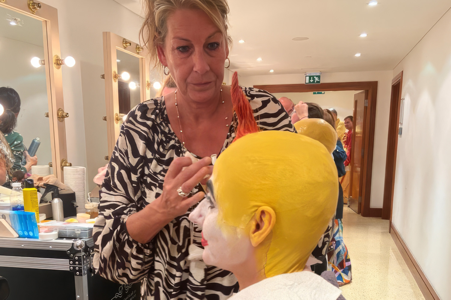 Makeup artist applying paint to a bald-cap headpiece backstage